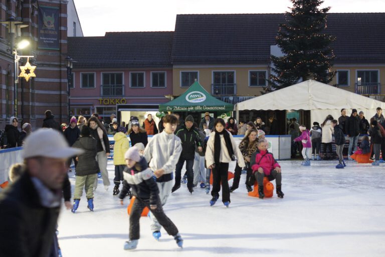 Das Bild zeigt die Eisbahn, auf der viele Kinder, Frauen und Männer ihre Runden drehen.