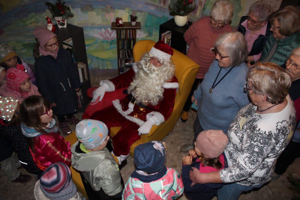 Der Weihnachtsmann sitz in seinem Selle, in den er geschlafen hatte. In umringen die Kinder und die Senioren.