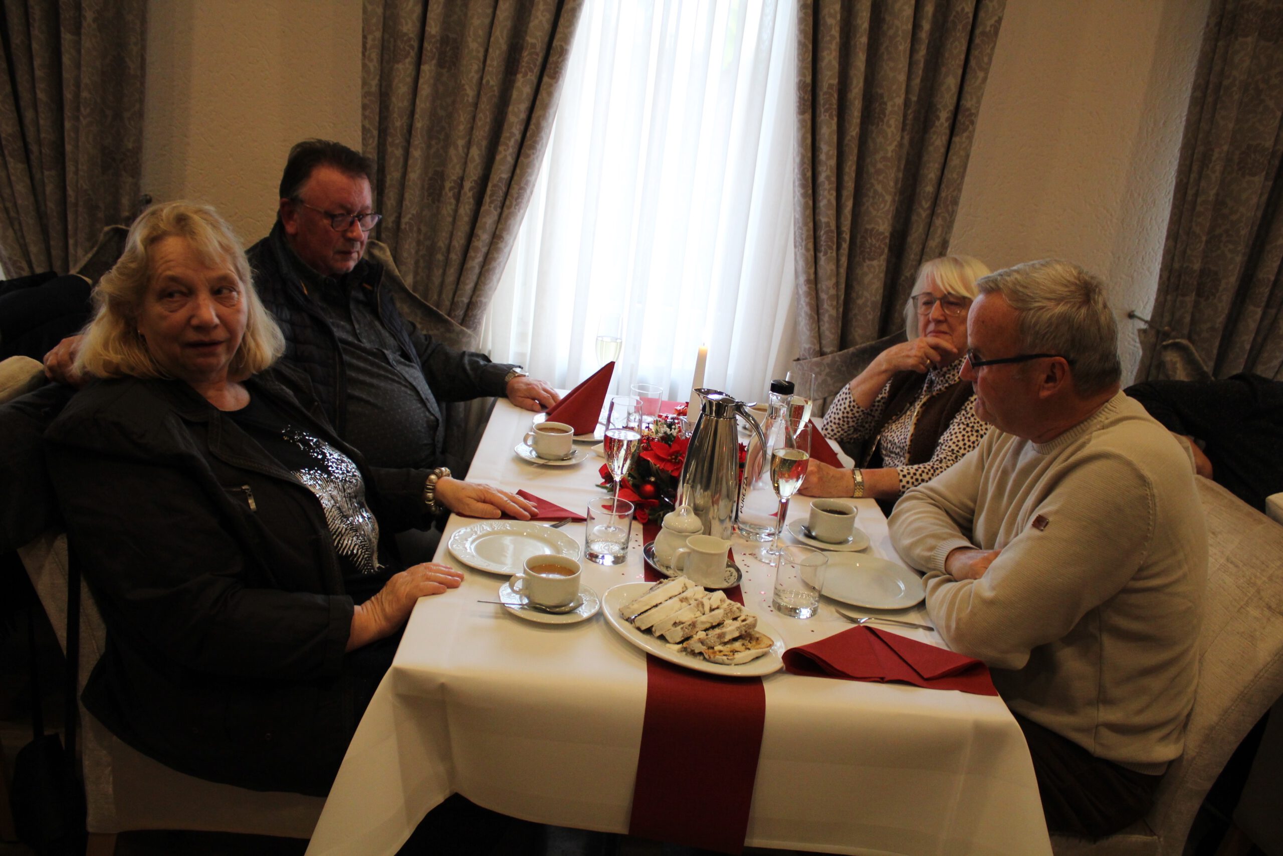 In gemütlicher Runde sitzen zwei Paare am weihnachtlich geschmückten Tisch.
