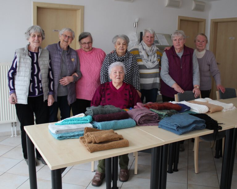 Frauen der Handarbeitsgruppe Güstrow stehen hinter einem Tisch, auf dem die bereits fertigen Schals leigen.
