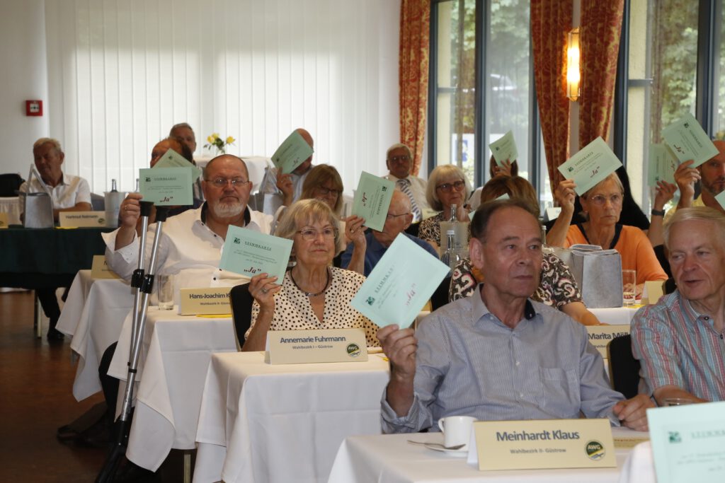 Das Foto zeigt Vertreter, die an Tischen in Parlamentsbestuhlung sitzen, bei der Abstimmung zu einem Tagesordnungspunkt.