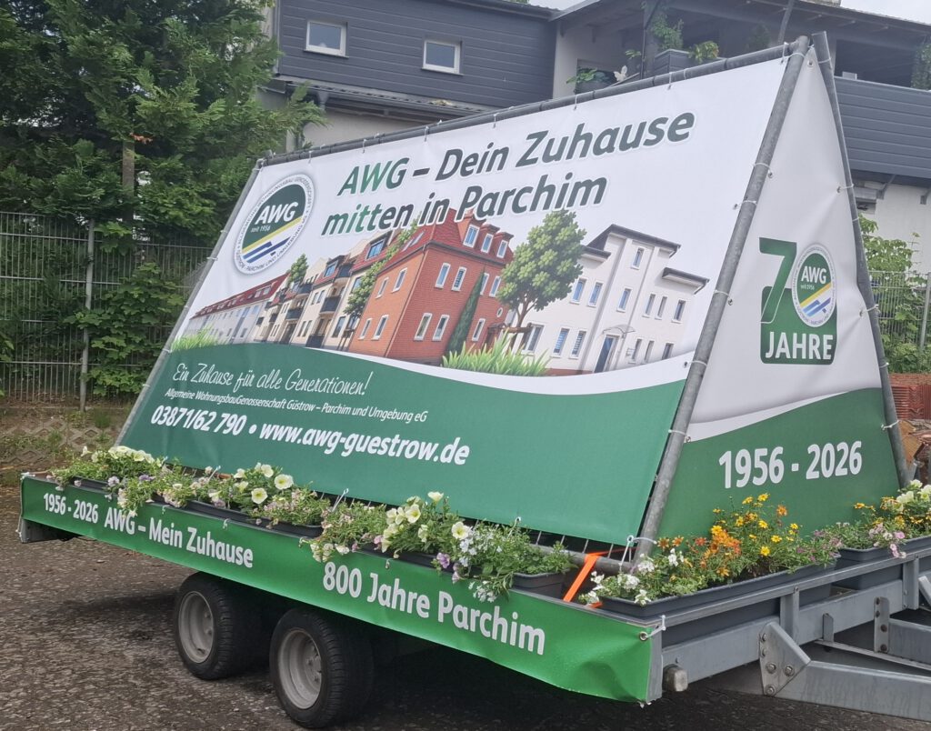 Auf dem Bild ist der AWG-Wagen zu sehen. Er ist mit bepflanzten Blumenk&auml;sten dekoriert. Mittig sind in Dachform Plakate zu sehen. Sie &uuml;bermitteln die Botschaft, dass die AWG fester und verl&auml;sslicher Partner f&uuml;r alle Parchimer ist.