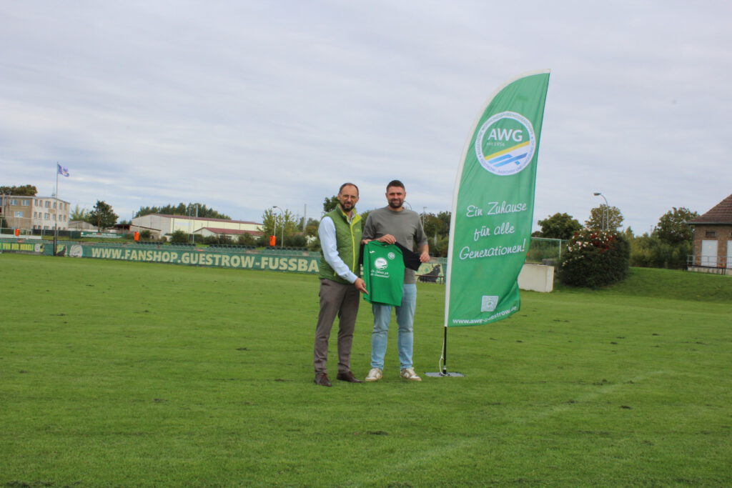 Das Foto zeigt AWG-Vorstandsvorsitzenden Marco Mischinger und GSC-Abteilungsleiter Oliver Diehl nach der Vertragsunterzeichnung auf dem Rasen des Stadions der Freundschaft in Güstrow. In ihren Händen halten sie eines der neuen Trikots, die dank einer Spende der AWG für die E1-Jugend angeschafft werden konnten.